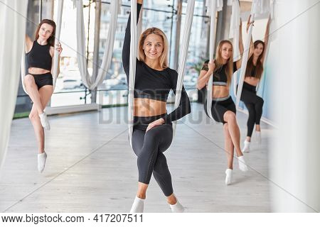 Group Of Female Are Doing Fly Yoga Exercises In Fitness Training White Gym Loft Classroom. Intense F