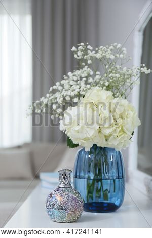 Stylish Catalytic Lamp With Beautiful Bouquet On White Table In Living Room. Cozy Interior