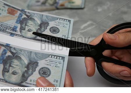 Counterfeiter Cutting Dollar Banknotes With Scissors At Grey Marble Table, Closeup. Fake Money