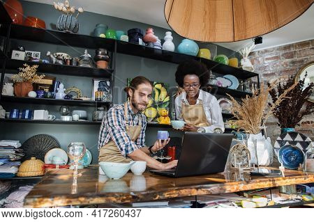 Two Multicultural People Working On Modern Laptop During Inventory Process At Decor Store. Young Cau