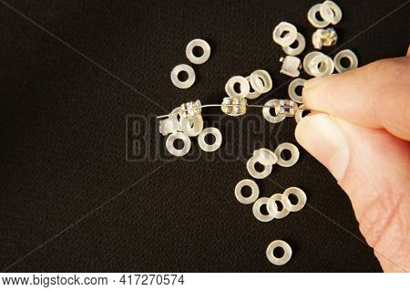 Dental Concept. Fingers Hold Metal Braces And Elastic Bands For Braces On Black Background. Copy Spa