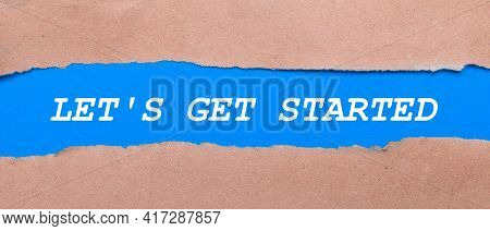 A Strip Of Blue Paper With The Words Let Is Get Started Between The Brown Paper. View From Above