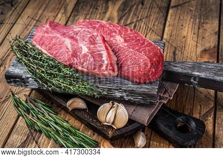 Raw Shoulder Top Blade Beef Meat Steaks On A Wooden Butcher Board With Herbs. Wooden Background. Top