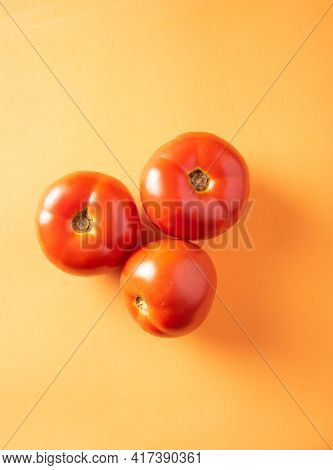 Tomatoes, Three Tomatoes Arranged On An Orange Surface, Top View.