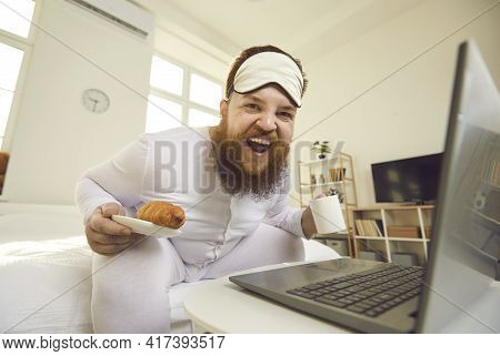 Happy Fat Man In Pajamas Sitting On Bed In The Morning, Enjoying Breakfast And Laughing