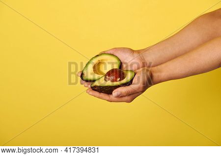 Closeup Of Hands Holding Two Halves Of Ripe Ready-to-eat Avocado. Closeup On Yellow Background With 