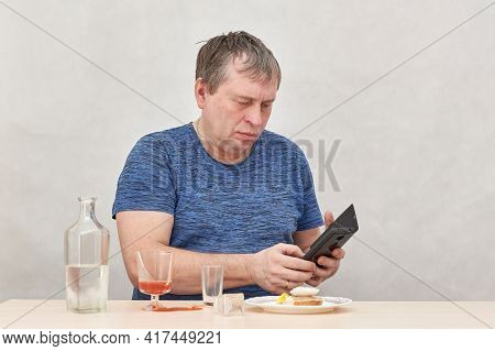 A Drunken Business Man With A Smartphone Sits Alone At A Table With Alcohol.