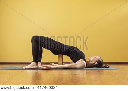 Woman Practicing Yoga, Doing Dvipada Pithasana, Half Bridge Pose With A Wooden Block Under The Lower
