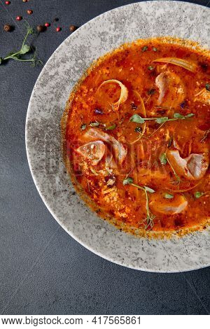 Russian cuisine - Solyanka Soup on dark textured table. Spicy and sour soup with meat slice and vegetables. Ceramic bowl on dark background. Top view