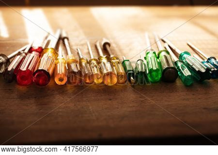Tools of the trade. Many kinds of screw drivers with colorful grips on a work bench, with incoming window light.