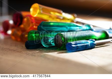 Tools of the trade. Many kinds of screw drivers with colorful grips on a work bench, with incoming window light.
