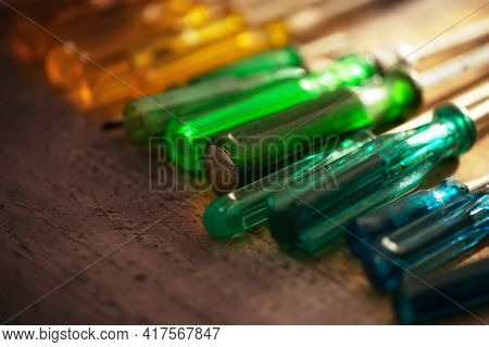 Tools of the trade. Many kinds of screw drivers with colorful grips on a work bench, with incoming window light.