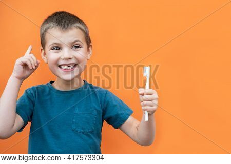 Boy Without Milk Upper Tooth In Blue T-shirt Holds Toothbrush In His Mouth On The Orange Background.