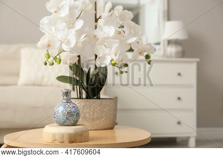 Stylish Catalytic Lamp With Orchid On Wooden Table In Living Room, Space For Text. Cozy Interior