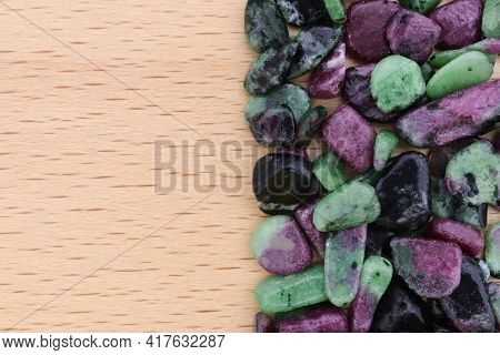 Ruby Zoisite Heap Jewel Stones Texture On Half Light Varnished Wood Background. Place For Text.