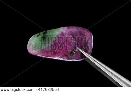 Ruby Zoisite Jewel Stone Texture In Tweezers On Black Background. Macro Closeup.