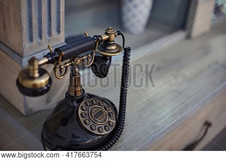 An old Fashioned rotary telephone sitting on a desk. This is a selective focus photo of a vintage piece of communication technology with copy space