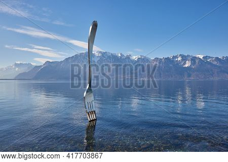 Vevey, Switzerland - Circa 2021: Huge steel fork art installation in Lake Geneva part of the Alimentarium food museum in Vevey, rippling water surface