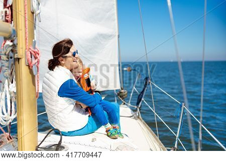 Mother And Baby Boy Sail On Yacht In Sea. Family Sailing On Boat. Mom And Kid In Safe Life Jacket Tr