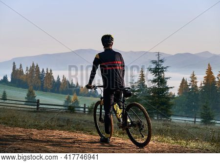 Back View Of Male Cyclist In Cycling Suit Standing With Bike In The Morning. Man Bicyclist Enjoying 