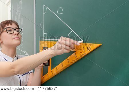 School Teacher Young Woman In The Class At The Blackboard Draws A Triangle With A Ruler. Portrait. C