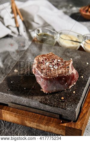 Fillet Steak - Cooking Filet Mignon Beef Steak on Hot Steak Stone with Salt and Pepper. Raw Beef Meat with Steam from Hot Stone