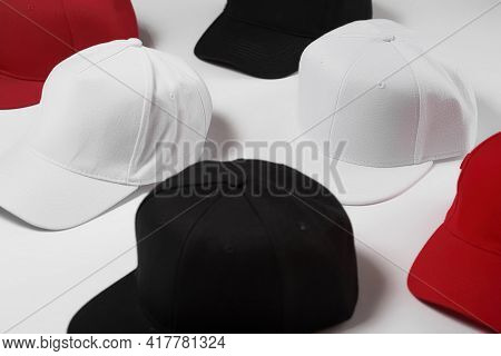 Closeup Shot Of Many Baseball Snapback Hats In Different Colors Black, White And Red Laid Out On Whi