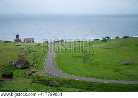 Road Leading To Faroese Village Of Trollanes Viewed From A Hill Nearby. Green Hills, Cloudy, Misty W