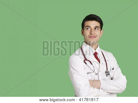 Mężczyzna lekarz w fartuchu stałego z rękami skrzyżowanymi patrząc na zielonym tle
