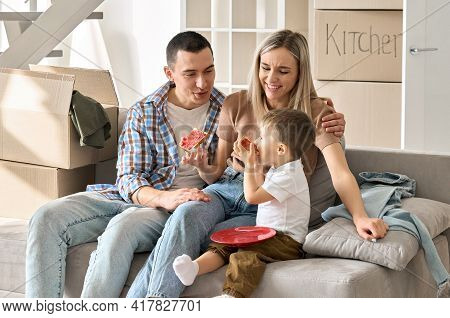 Happy Young Family Sitting On Sofa With Kid Feeding With Bread And Jam. Joyful Family In Living Room