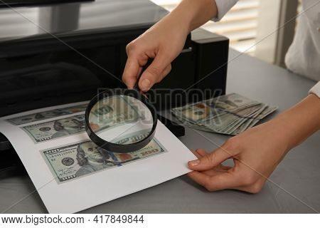 Counterfeiter Examining Sheet Of Paper With Dollar Banknotes At Table Indoors, Closeup. Fake Money C