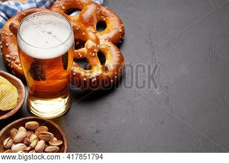 Lager beer mug, nuts, potato chips and fresh baked homemade pretzel with sea salt on stone table. Classic beer snack. With copy space
