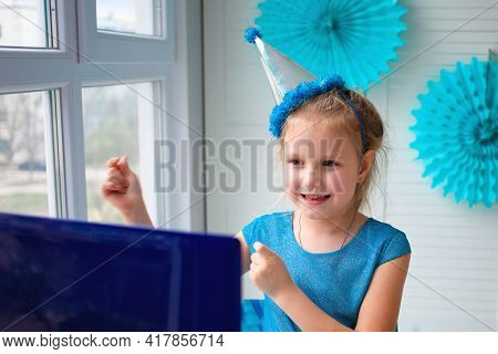 A Little Girl, Curves And Laughs In Front Of A Laptop In A Cap. Celebrates Birthday Via Internet In 