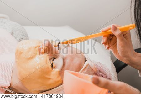 Moisturizing The Skin At The Spa, The Beautician Applies A Gold Mask To The Client's Face.