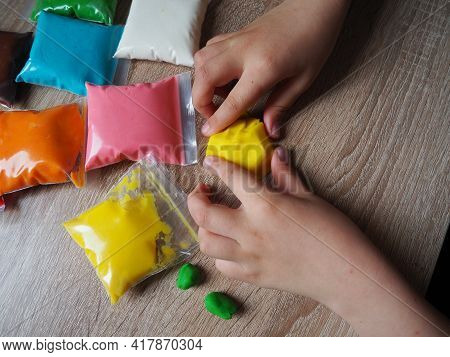 Children's Hands Crumple Soft Plasticine. Packages With Plasticine Are On The Table. Creativity For