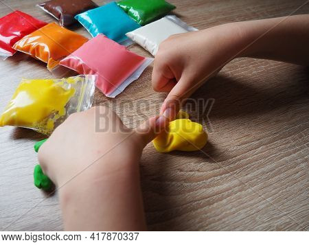 Children's Hands Crumple Soft Plasticine. Packages With Plasticine Are On The Table. Creativity For