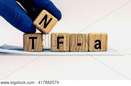 Text Tnf-a Made From Wooden Cubes. Hands In A Blue Glove.