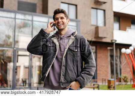 Smiling young white man in casual cothes using mobile phone outdoors in the city, walking