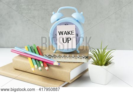 Wake Up Word On Alarm Clock With Colored Pencils And Gray Background. Learning And Education Concept