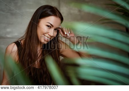 Beautiful Young Woman Closeup Portrait Through Green Leaves Of A Flower On A Gray Wall Background