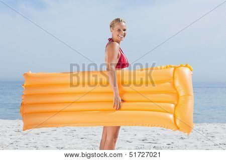 Smiling woman walking on beach with lilo