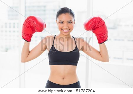 Lovely dark haired model in sportswear wearing red boxing gloves in bright fitness studio