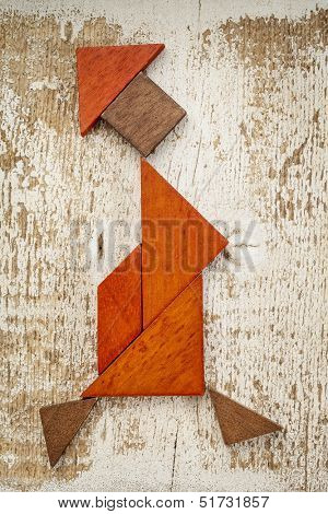 abstract figure of a walking woman built from seven tangram wooden pieces, a traditional Chinese puzzle game; rough white painted barn wood background