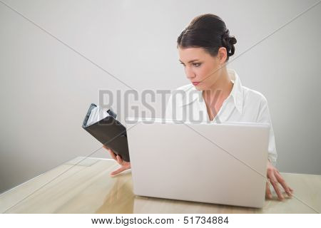 Gorgeous businesswoman working on laptop holding datebook in bright office