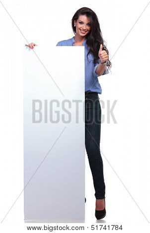 full length picture of young casual woman holding a big empty pannel and showing thumb up to the camera while smiling. on white background