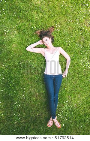 Cute brunette woman lying on a lawn smiling at the camera