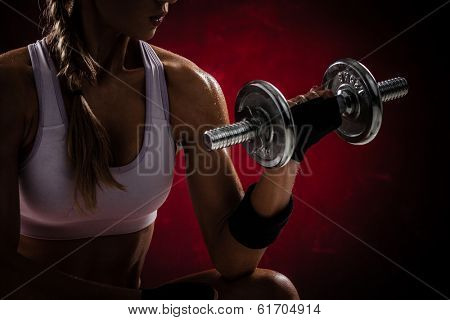 Brutal athletic woman pumping up muscles with dumbbells on red background