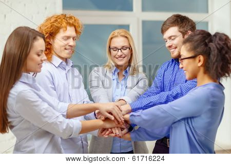 business, office, gesture and startup concept - smiling creative team with hands on top of each other sitting in office