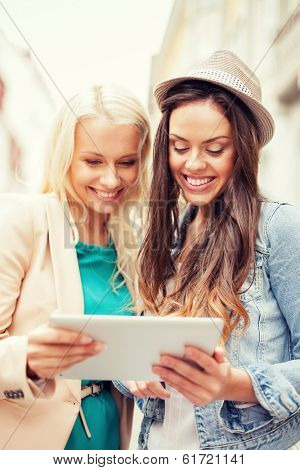 holidays and tourism concept - beautiful girls toursits looking into tablet pc in the city