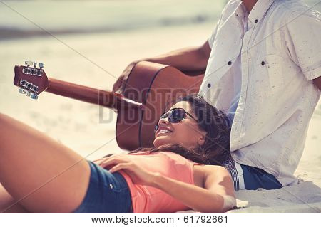 Cute hispanic couple playing guitar serenading on beach in love and embrace